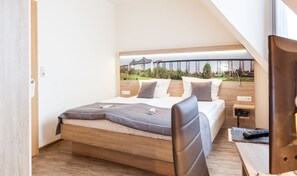 A bedroom with a bed, a desk, and a chair. There is a window with a view of a bridge and trees. - Hotel Hansen (Rendsburg)