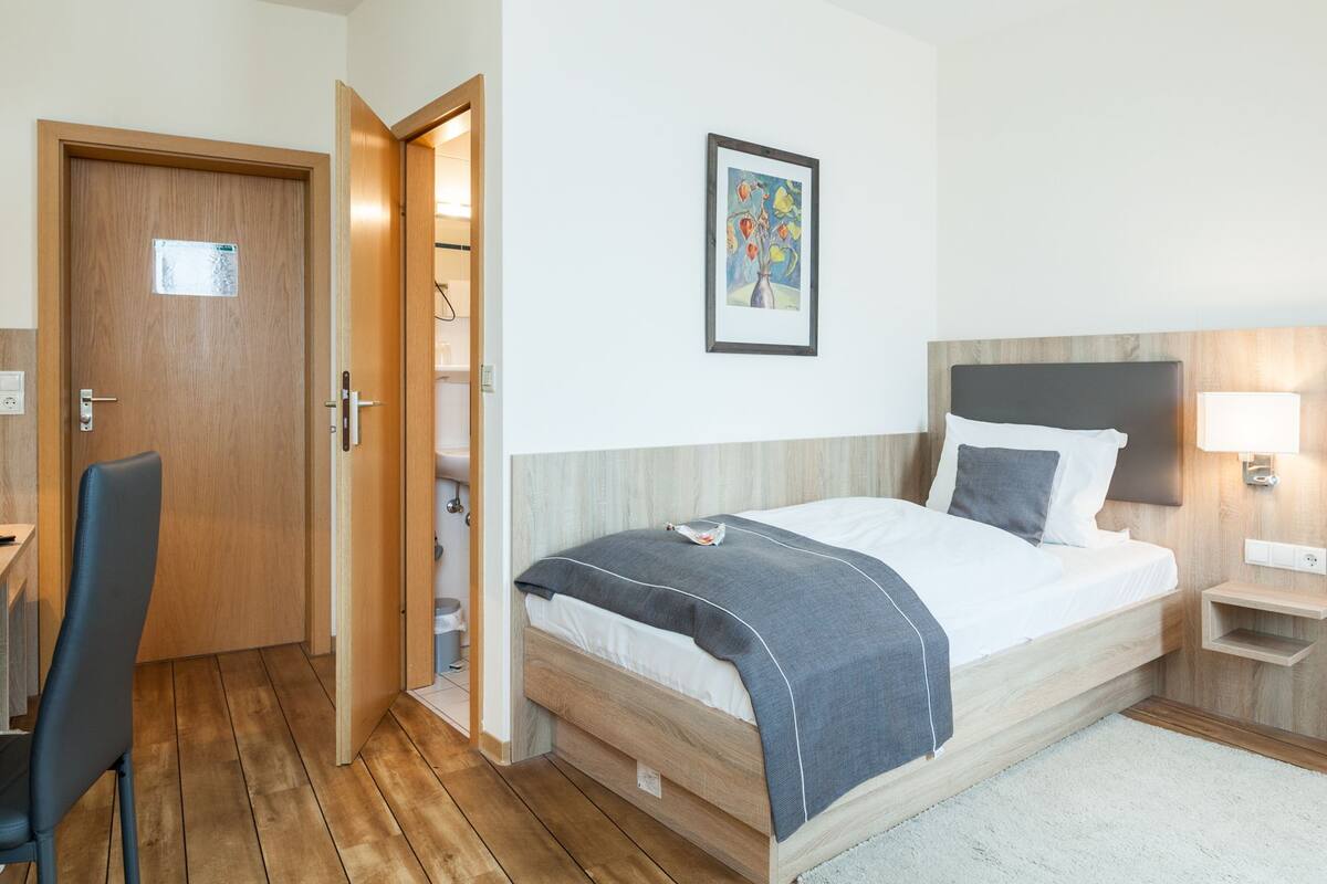 Ein Hotelzimmer mit Bett, Schreibtisch, Stuhl, Nachttisch und einem Bild an der Wand.
