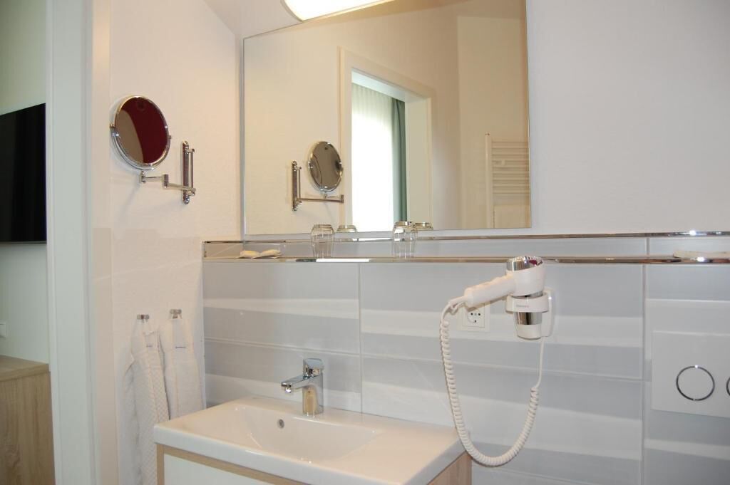 Un baño con lavamanos, dos espejos, secador de pelo y toallero.