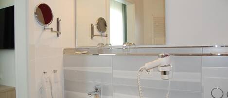 Un baño con lavamanos, dos espejos, secador de pelo y toallero.