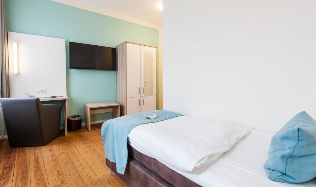 A hotel room with a bed, a desk, a chair, a wardrobe, and a television.