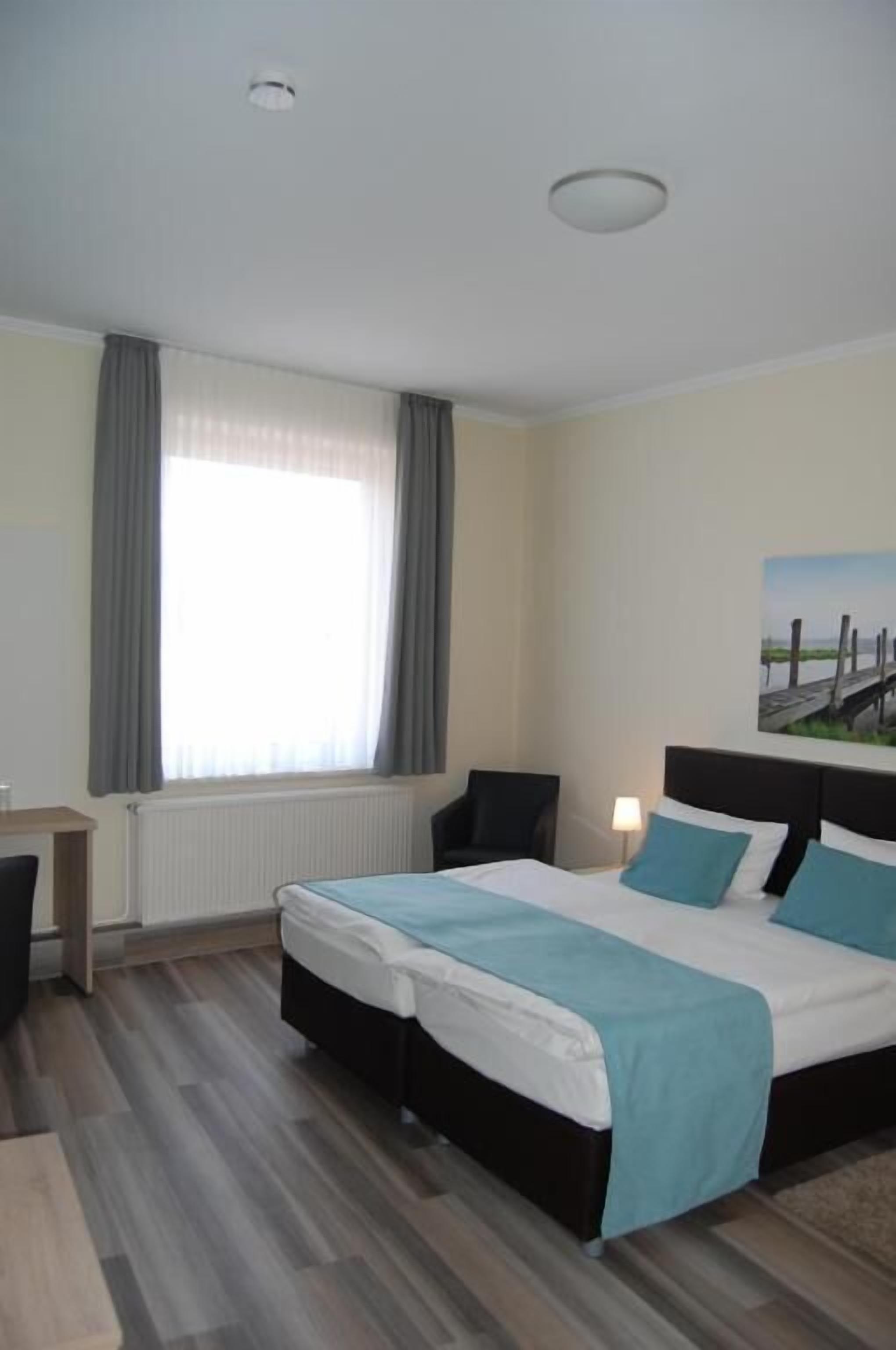 A hotel room with a large bed, a desk, a chair, and a window with curtains.