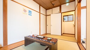 Une pièce de style japonais traditionnel, avec un sol recouvert de tatamis, une petite table en bois et un service à thé, des portes coulissantes et une petite fenêtre donnant sur un paysage agréable.