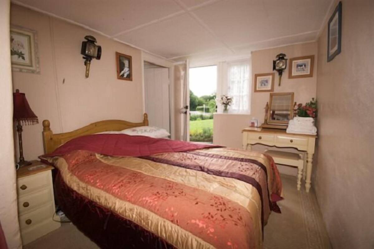 A bedroom with two beds, a nightstand, a dresser, and a window with a view of greenery.