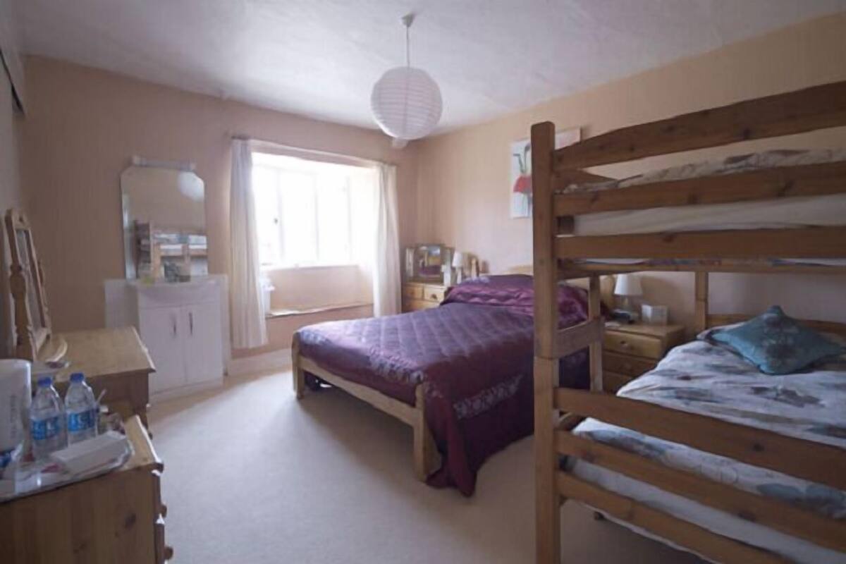 A bedroom with a bunk bed, a desk with a chair, a wardrobe, and a window with curtains.