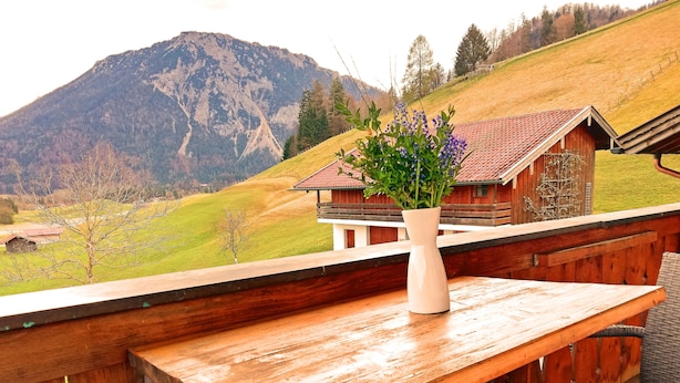 A wooden table with a white vase of flowers on a balcony overlooking a mountainous landscape. - Apartment Beim Raffner (Ruhpolding)