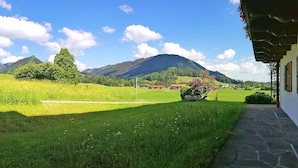 A rural landscape with a grassy field, a small building, and mountains in the background. - Apartment Beim Raffner (Ruhpolding)