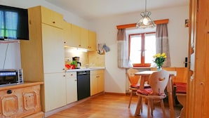 A compact kitchen with wooden cabinets, a microwave, a coffee maker, and a sink. There is a dining table with chairs and a vase with flowers. - Apartment Beim Raffner (Ruhpolding)