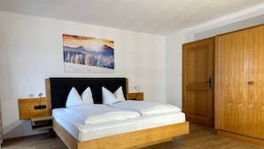 A bedroom with a wooden bed, white bedding, a nightstand, a wall-mounted painting, and a wooden wardrobe. - Apartment Beim Raffner (Ruhpolding)