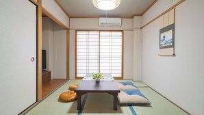 A traditional Japanese room with tatami flooring, a low table with a plant, sliding doors, and a hanging artwork. - YUYU House - Kohama Mei (Osaka)
