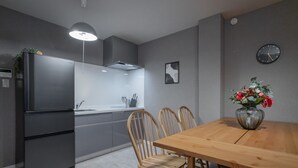 A modern kitchen with a built-in refrigerator, wooden chairs, a wooden dining table, and a vase with flowers on the table. - YUYU House - Kohama Mei (Osaka)