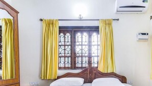 Une chambre d’hôtel avec un lit en bois, des rideaux jaunes, une fenêtre avec des barreaux en métal et un appareil de climatisation.