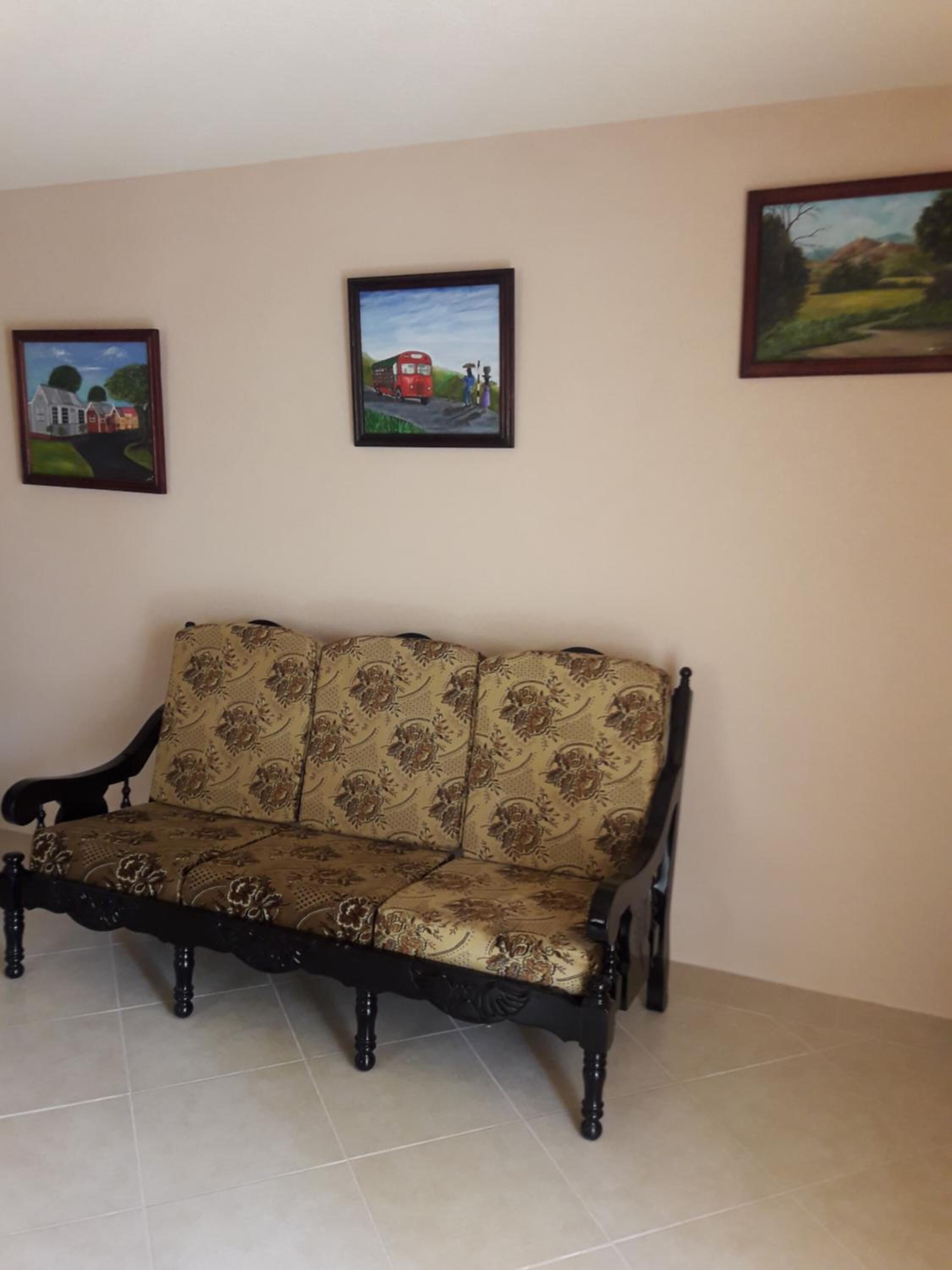 A room with a sofa, a painting of a rural scene, and another painting of a bus on the wall.