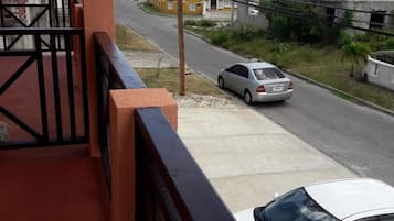 A balcony with a black railing overlooking a street with parked cars and buildings.