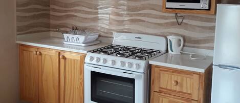 A kitchen with wooden cabinets, a stove, a microwave, and a refrigerator.
