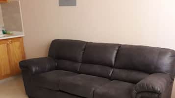 Un sofá de cuero marrón oscuro en una habitación con suelo de baldosas y un mueble de madera.