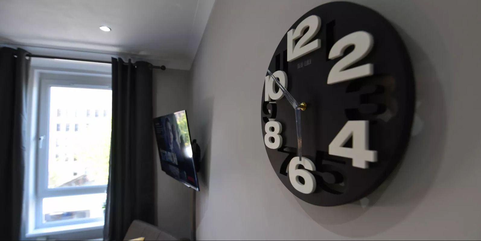 Une horloge murale au design moderne, un téléviseur à écran plat et une fenêtre avec des rideaux.