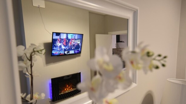 A living room with a television mounted on the wall, a fireplace, and a white armchair. - First - Slateford House Apartment (Edinburgh)