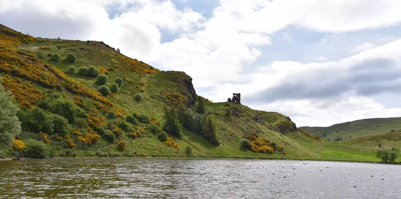 A coastal landscape with a hill, a body of water, and a ruined structure on the hill.