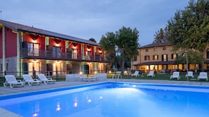 Une piscine avec des chaises longues, un bâtiment doté d’un balcon et un espace extérieur bien éclairé.