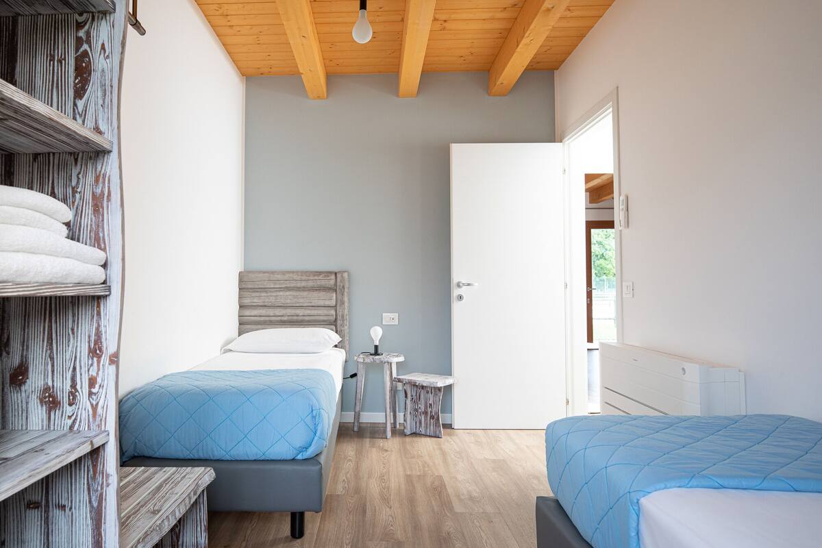 Een slaapkamer met twee bedden, een houten hoofdbord, een klein tafeltje en een deur naar een andere kamer.