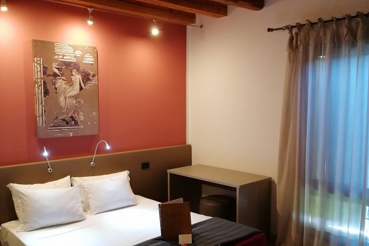 Een hotelkamer met een bed, nachtkastje en een poster aan de muur.