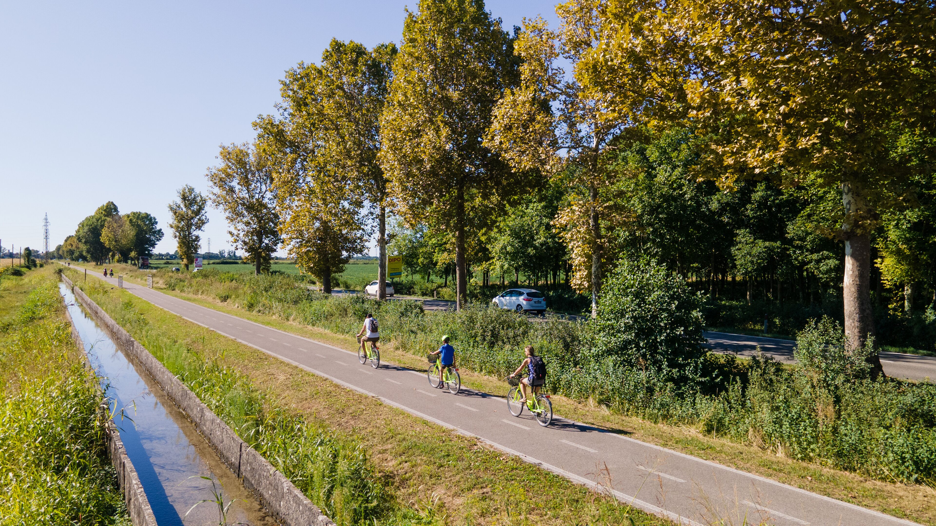 A paved path alongside a canal with cyclists and a road with cars.