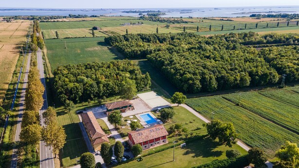 Vue aérienne d’une propriété dotée d’une piscine, d’un bâtiment à toit rouge et de champs environnants.