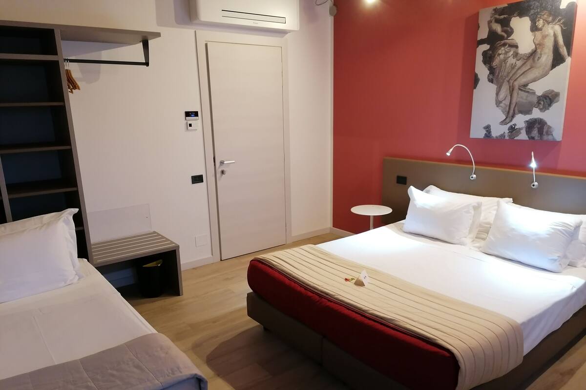 Een hotelkamer met twee bedden, een kledingkast, een tafeltje en een schilderij aan de muur.