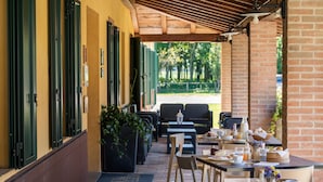 Un café en plein air avec des tables et des chaises, un mur en briques et un espace de repos abrité.