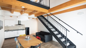 Une cuisine moderne avec des meubles blancs, une table à manger en bois et un escalier noir.