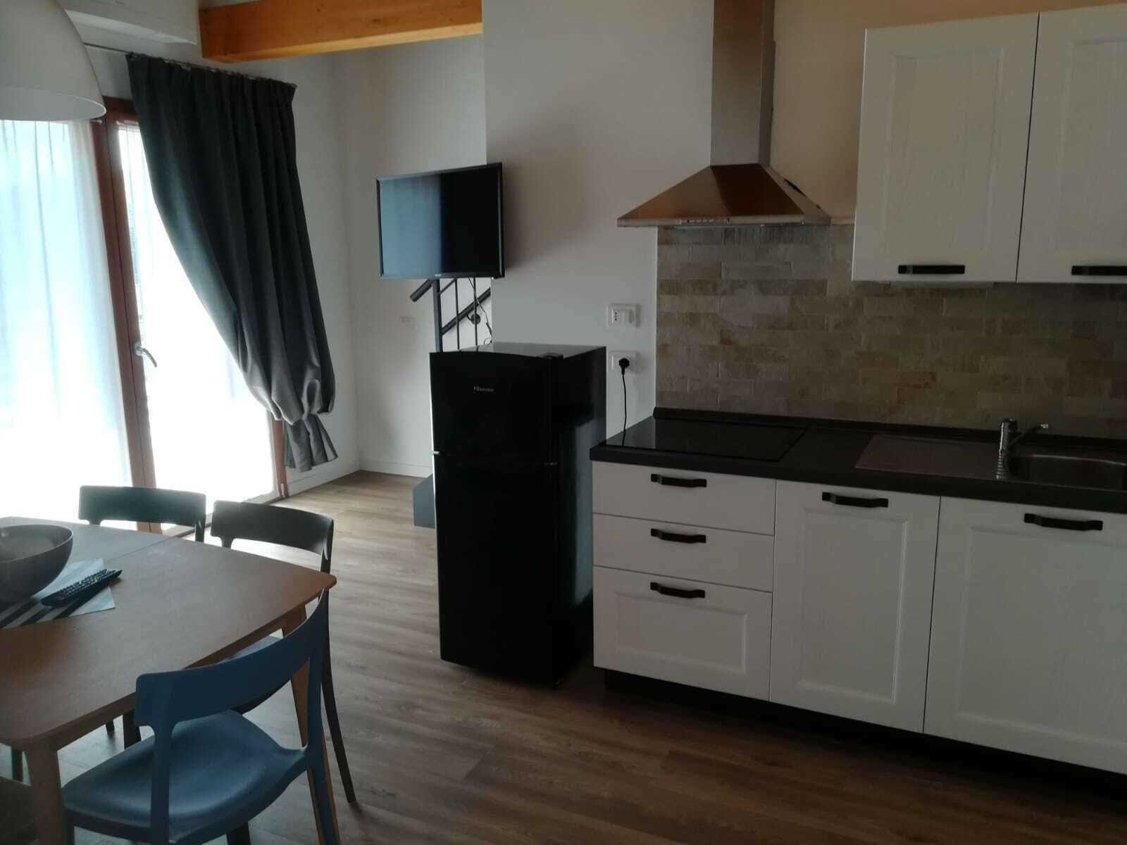 Une cuisine de taille réduite, avec des meubles blancs, un réfrigérateur noir et un téléviseur à écran plat fixé au mur.