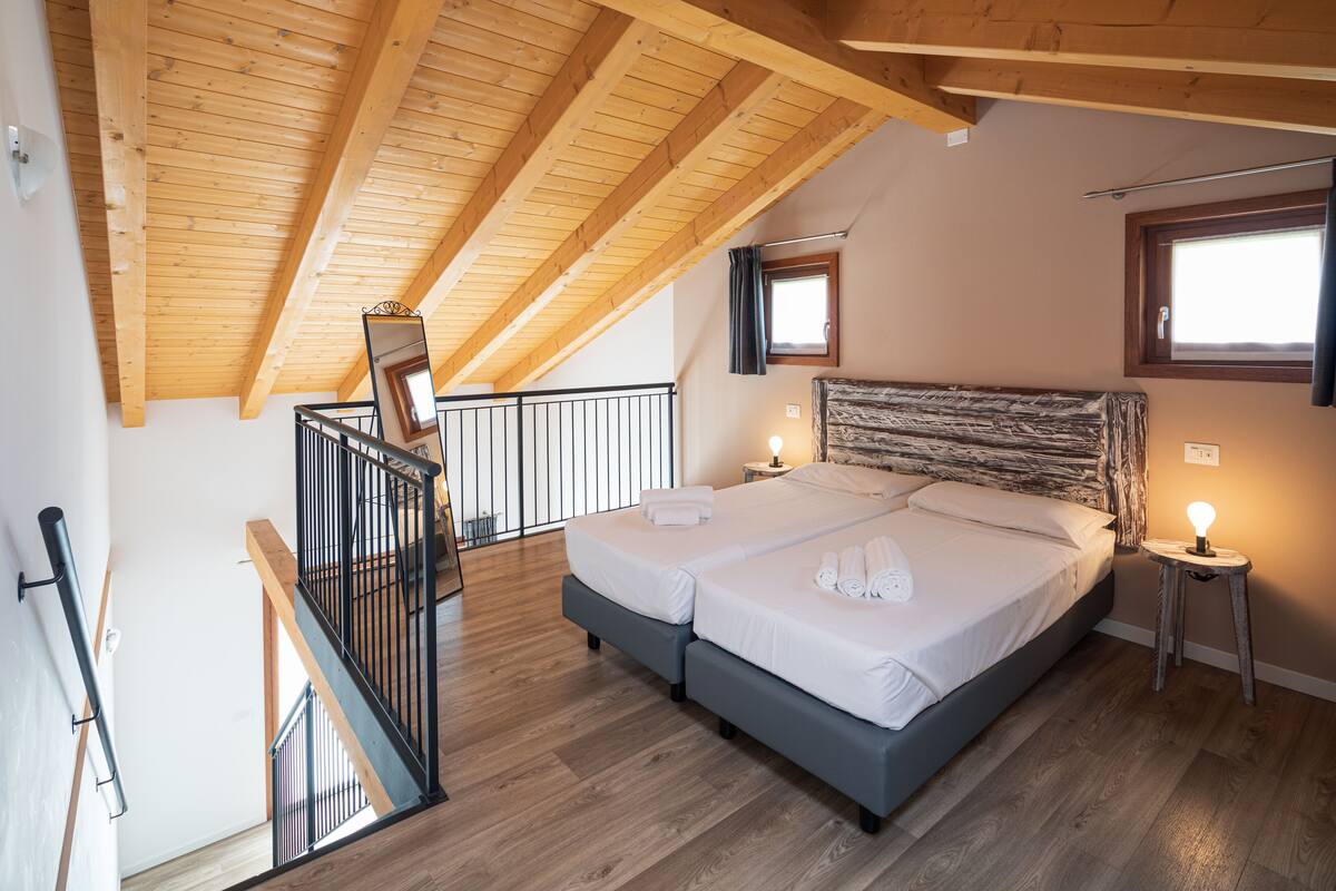 Een slaapkamer met een houten plafond, een bed met twee kussens, een nachtkastje en een raam.