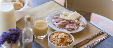 A breakfast setting with bread, cheese, ham, and cereal on a table.