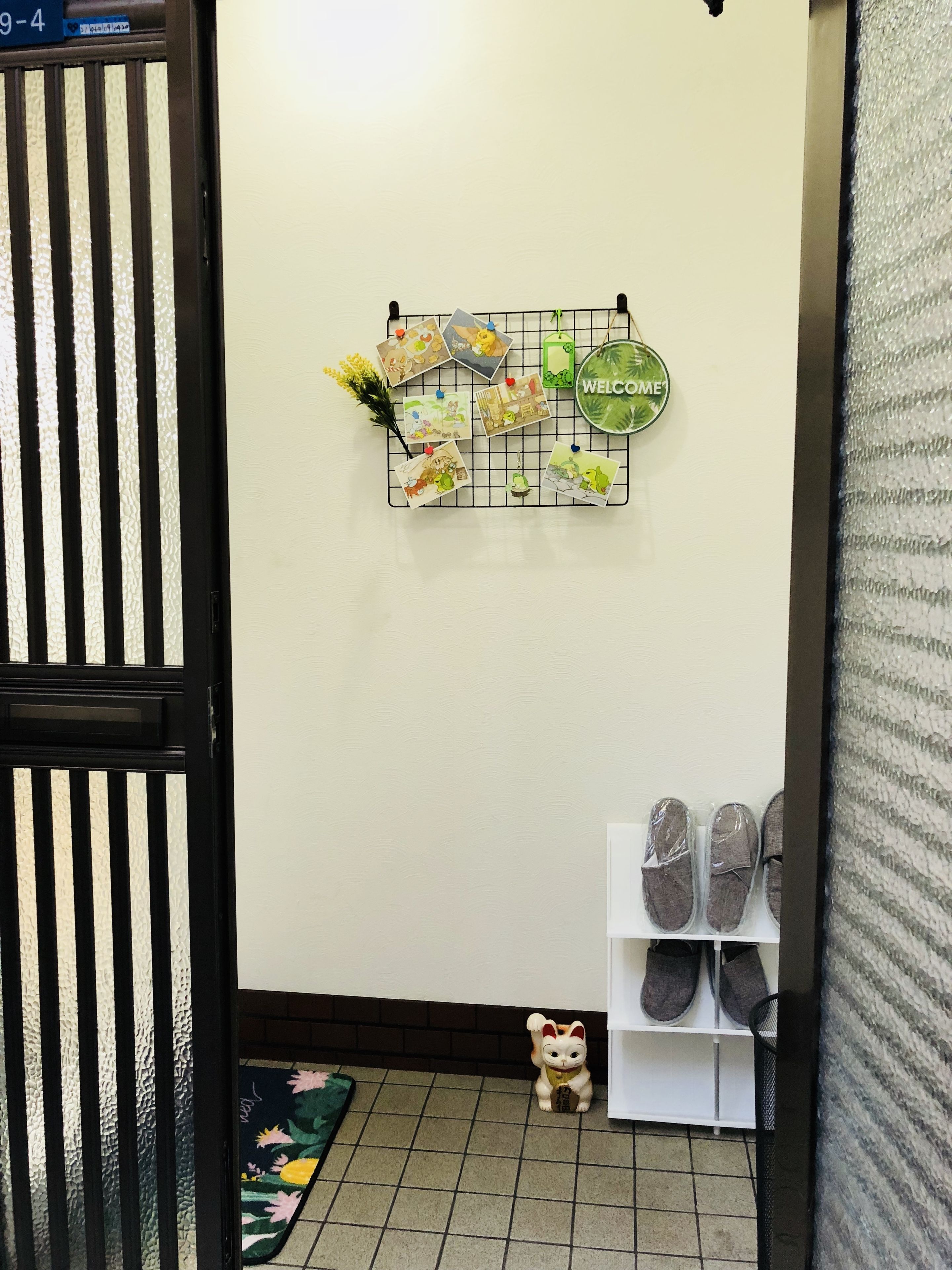 A hallway with a grid wall decoration, a shoe rack, and a small cat figurine on the floor.