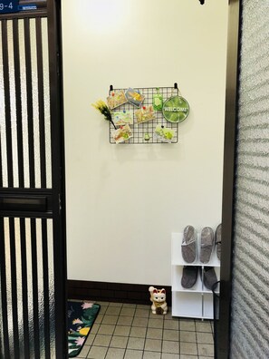 Un couloir décoré d’un motif géométrique mural, avec un meuble à chaussures et une petite figurine de chat posée sur le sol.