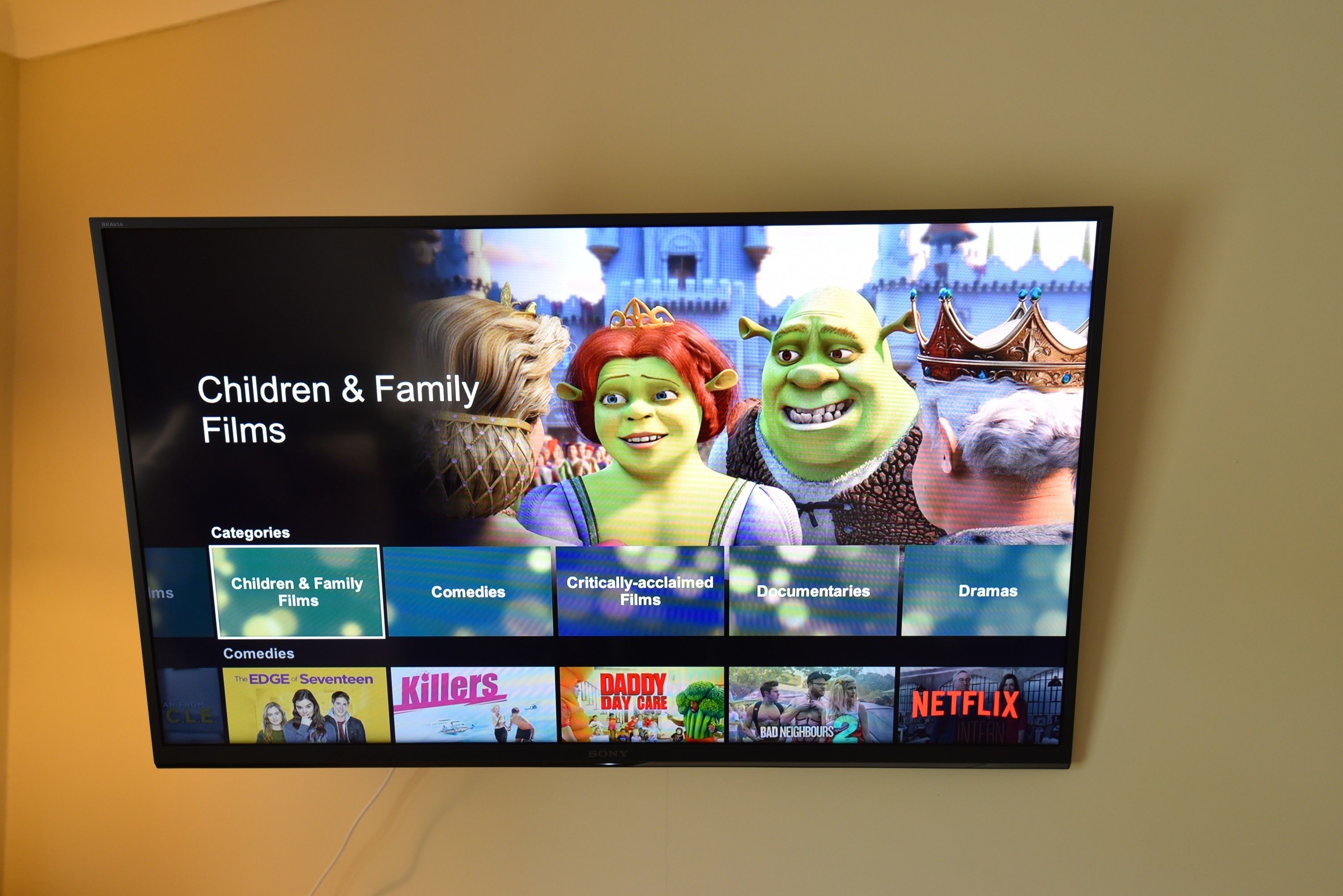 A television screen displaying a streaming service interface with categories like 'Children & Family Films' and 'Comedies'.