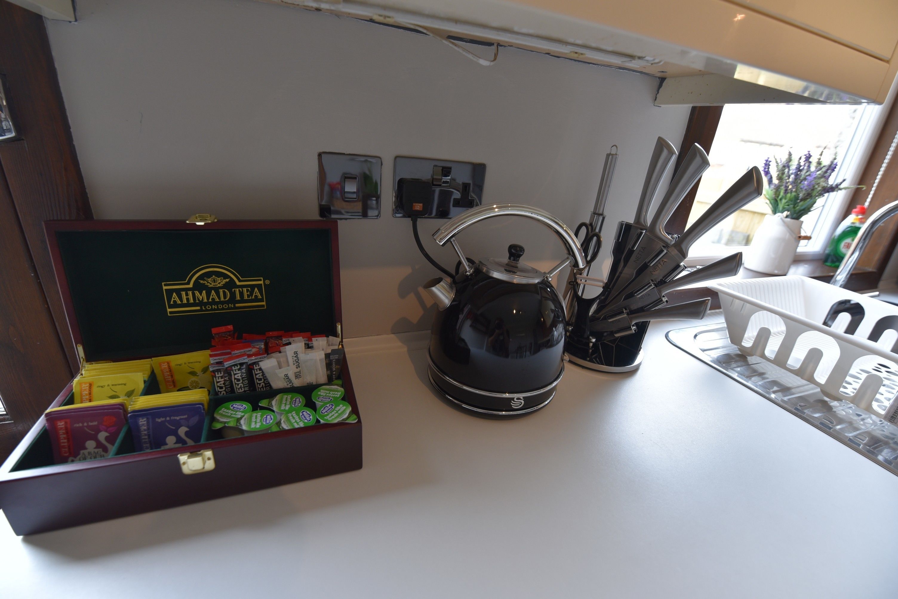 A kitchen counter with a tea box, a kettle, and kitchen utensils.