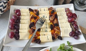Une assiette rectangulaire blanche, garnie de tranches de fromage blanc, de raisins et de fruits secs.