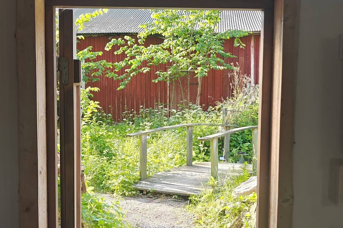 Une porte en bois donne sur un chemin de gravier, avec une grange rouge en arrière-plan.