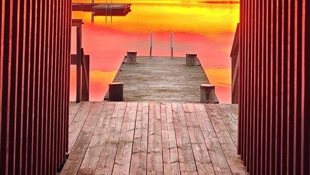 Een houten steiger die uitkomt bij een wateroppervlak, met een zonsondergang op de achtergrond.