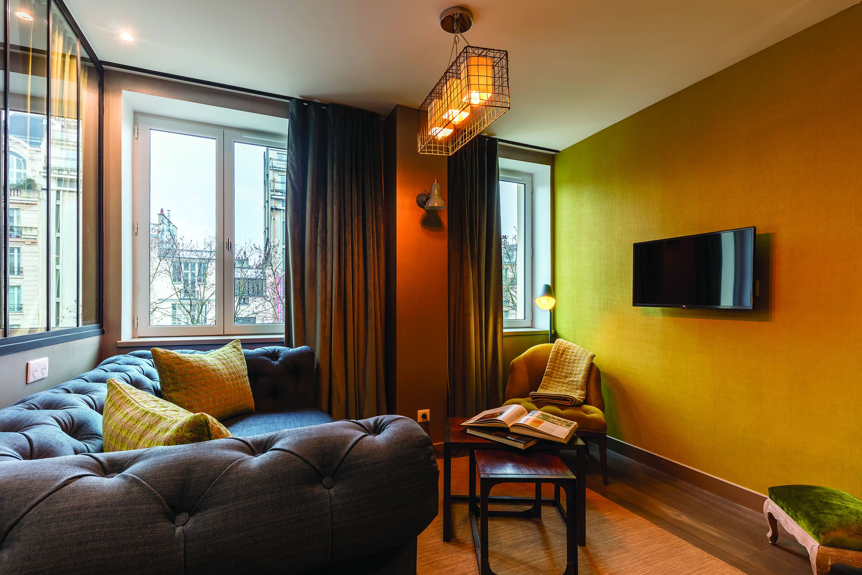 Un salon moderne avec un canapé, un fauteuil de lecture, un téléviseur à écran plat et une grande fenêtre avec des rideaux.