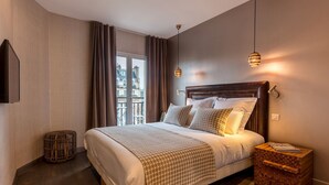 Un dormitorio moderno con una cama grande, una mesita de noche, un pequeño taburete redondo y vistas a edificios por la ventana.