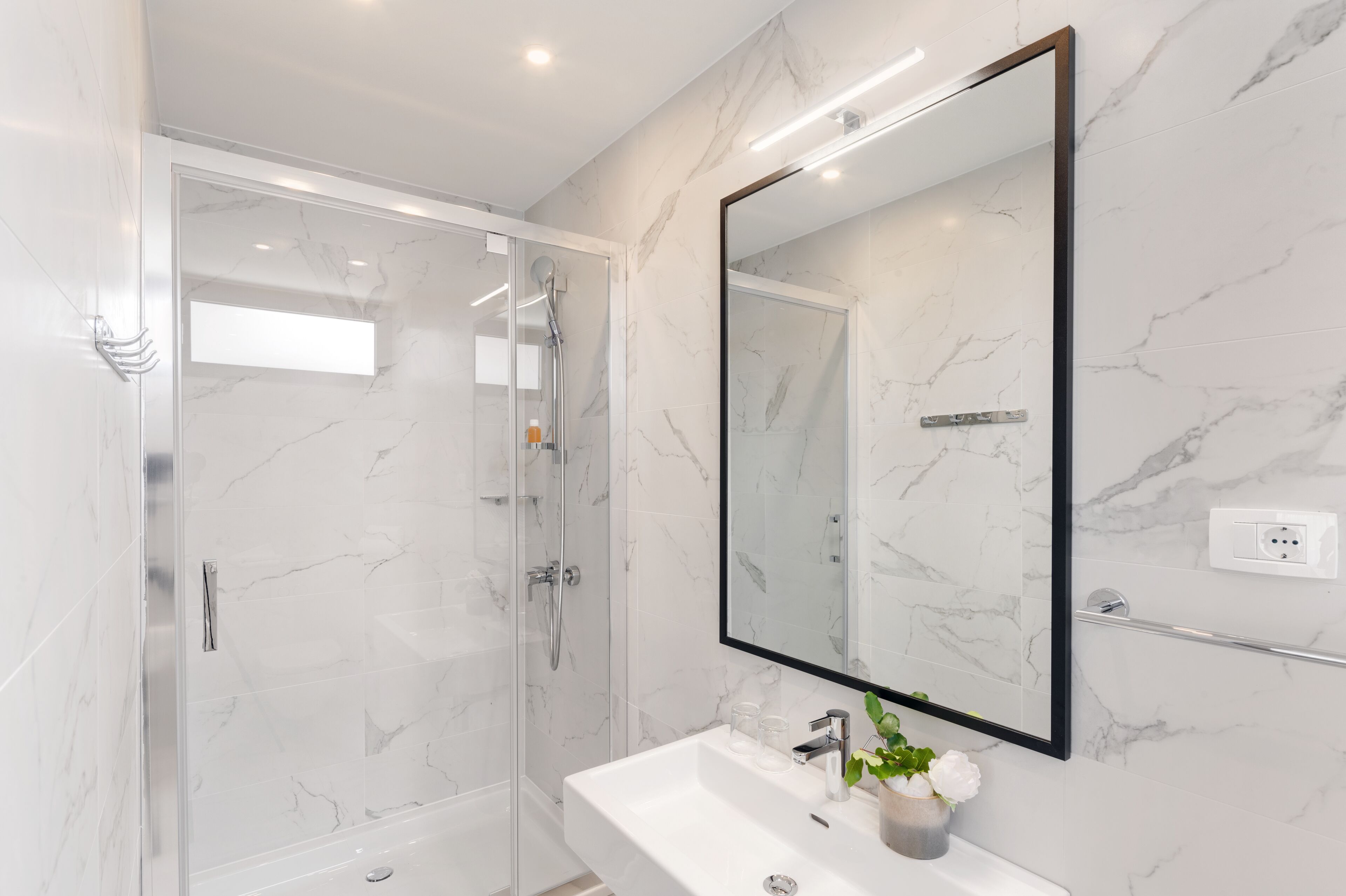A modern bathroom with a glass-enclosed shower, a white sink, and a large mirror.
