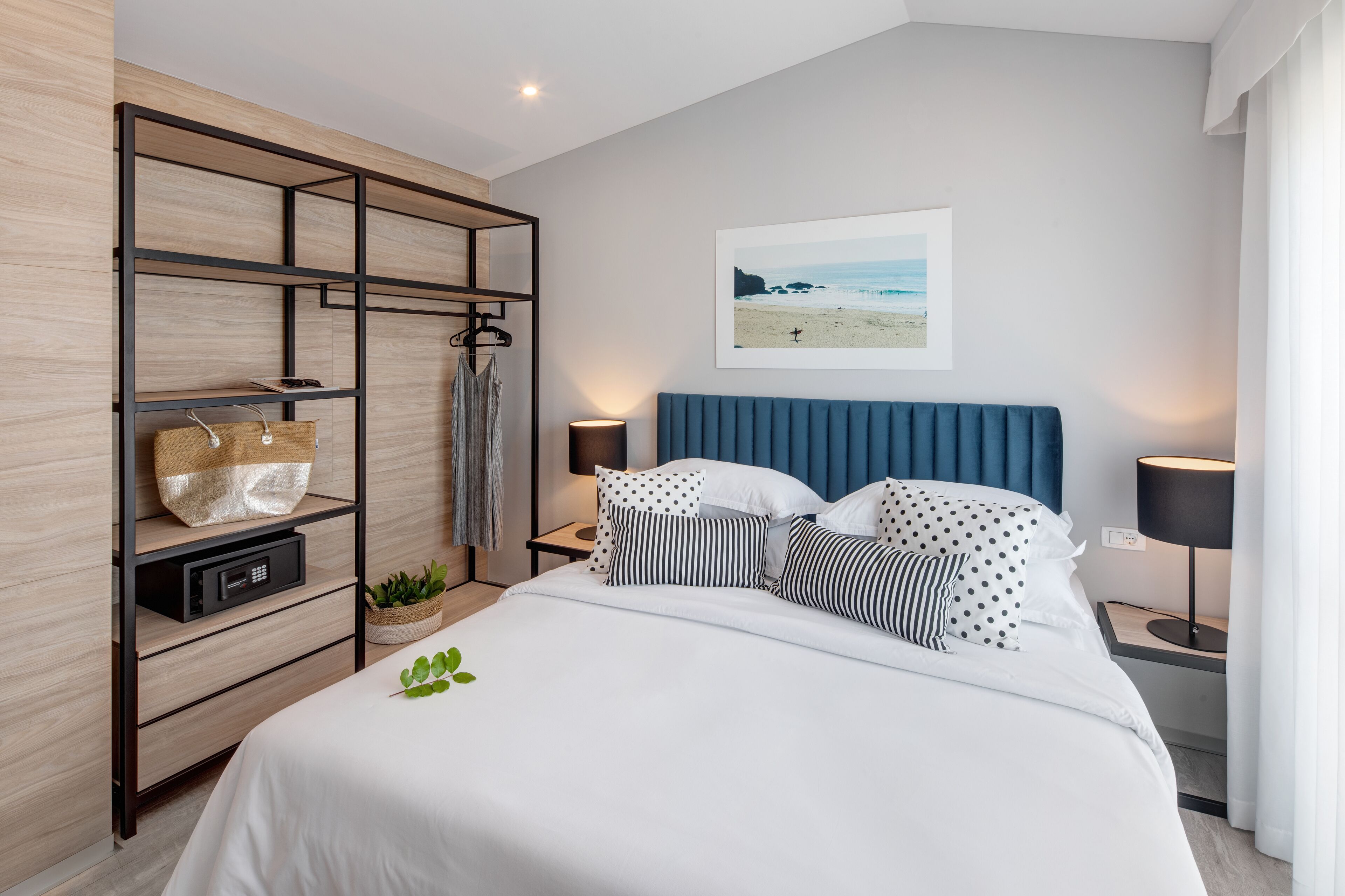 A modern bedroom with a bed, a wooden shelving unit, a wall-mounted picture, and bedside lamps.