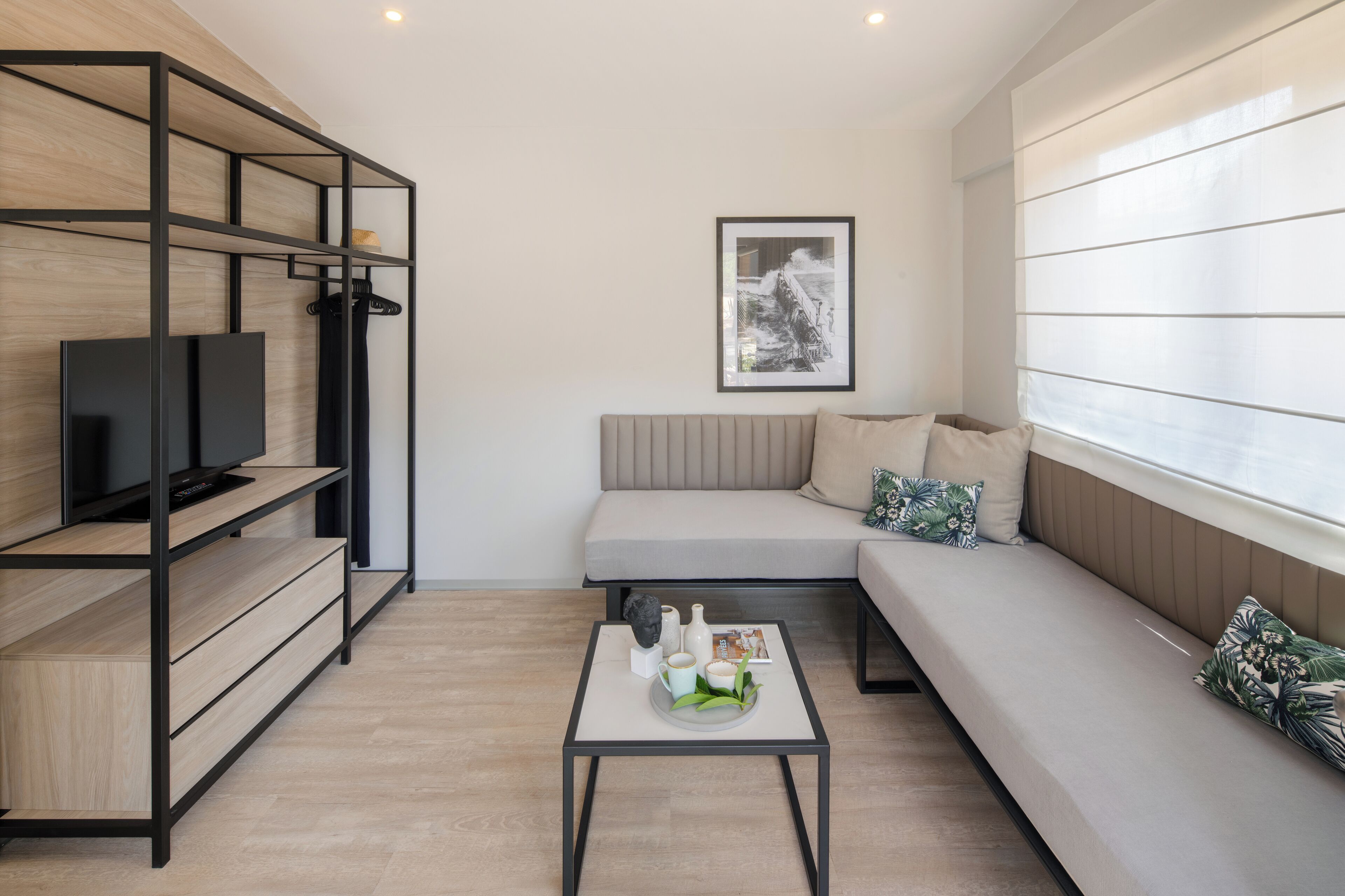 Una sala de estar moderna con un sofá, una mesa de centro, un televisor en un estante y un cuadro en la pared.