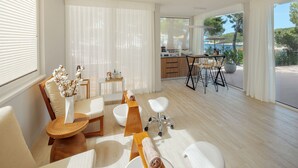 Una stanza moderna e luminosa con un'ampia finestra vista mare. Dispone di un tavolo da pranzo in legno con sedie, un divano bianco e un angolo cottura con bancone.