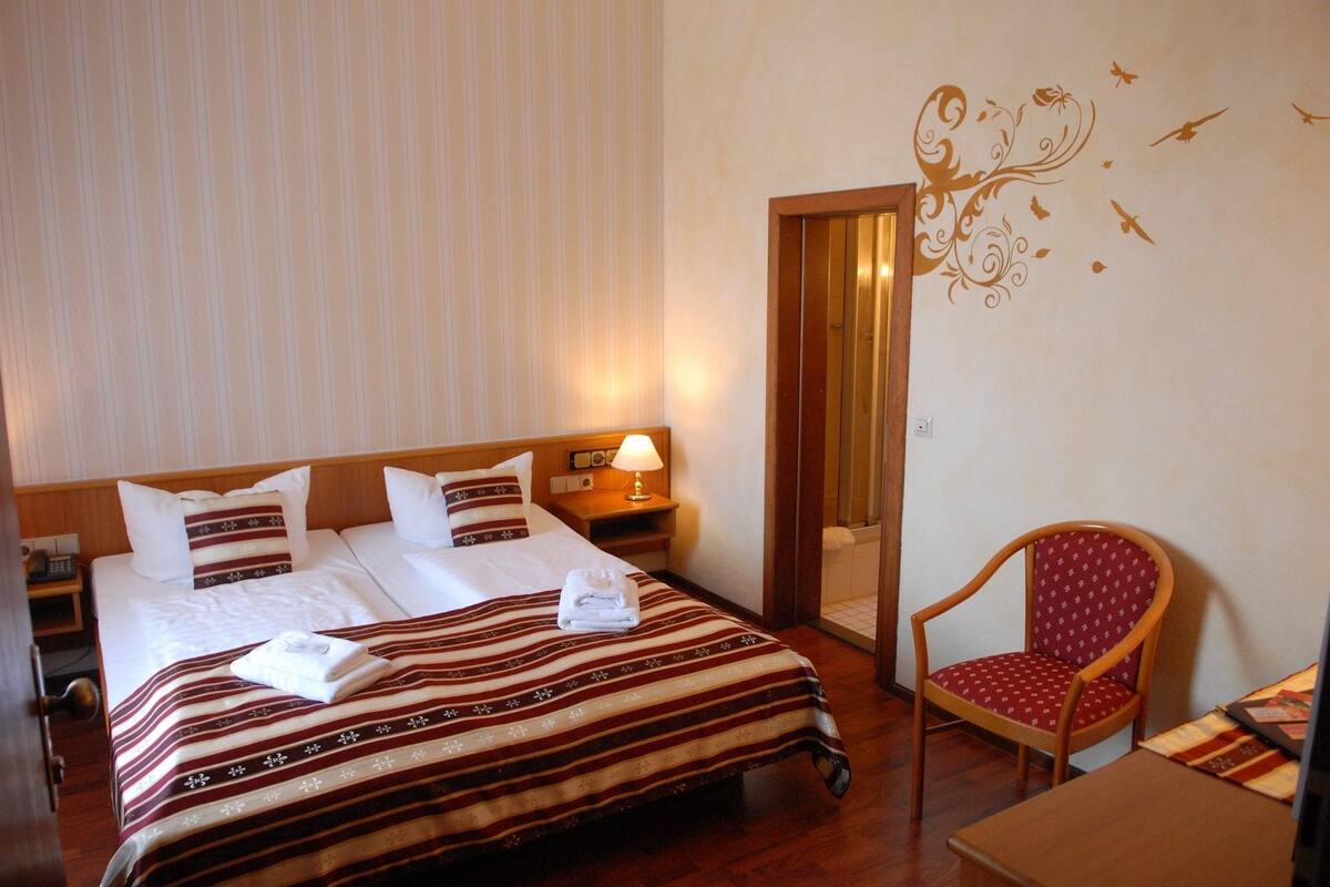A hotel room with a bed, a chair, a nightstand, and a mirror.