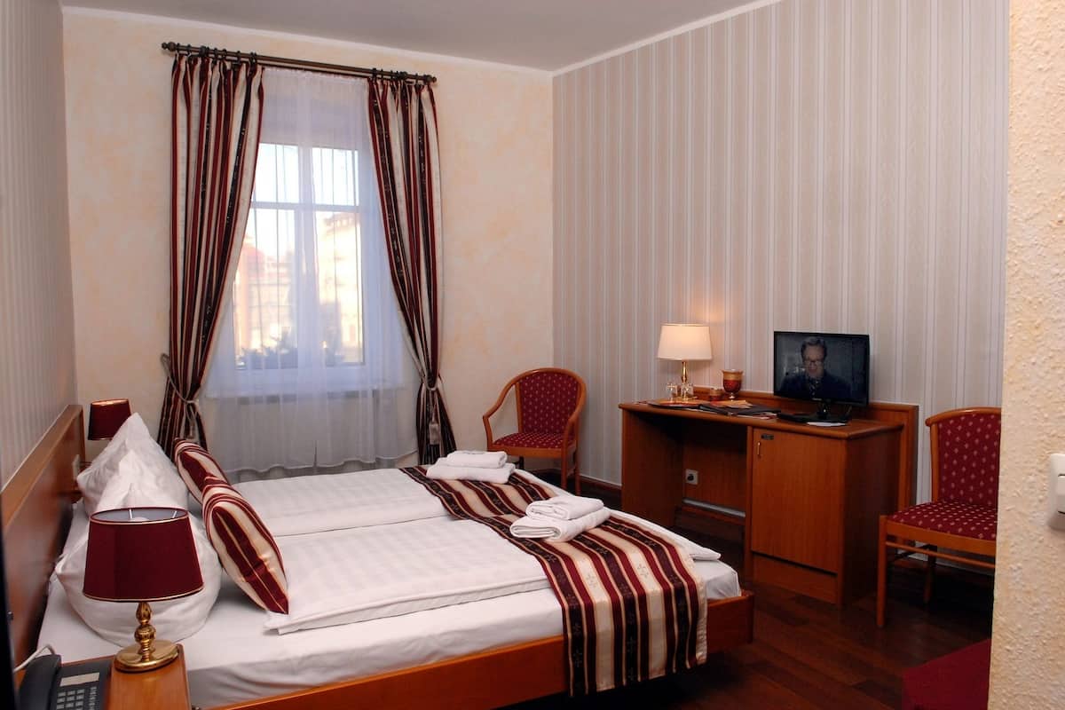 A hotel room with a bed, a desk, a chair, a TV, and a telephone.