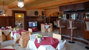 A restaurant with wooden paneling, a bar area, and a television screen. Tables are set with white tablecloths and red napkins. - Schwarzer Bär (Zittau)